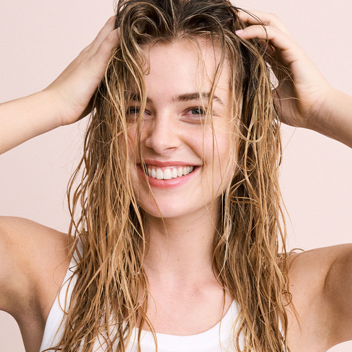 Woman with wet hair smiling and running her fingers through it, showcasing healthy shine and natural freshness.