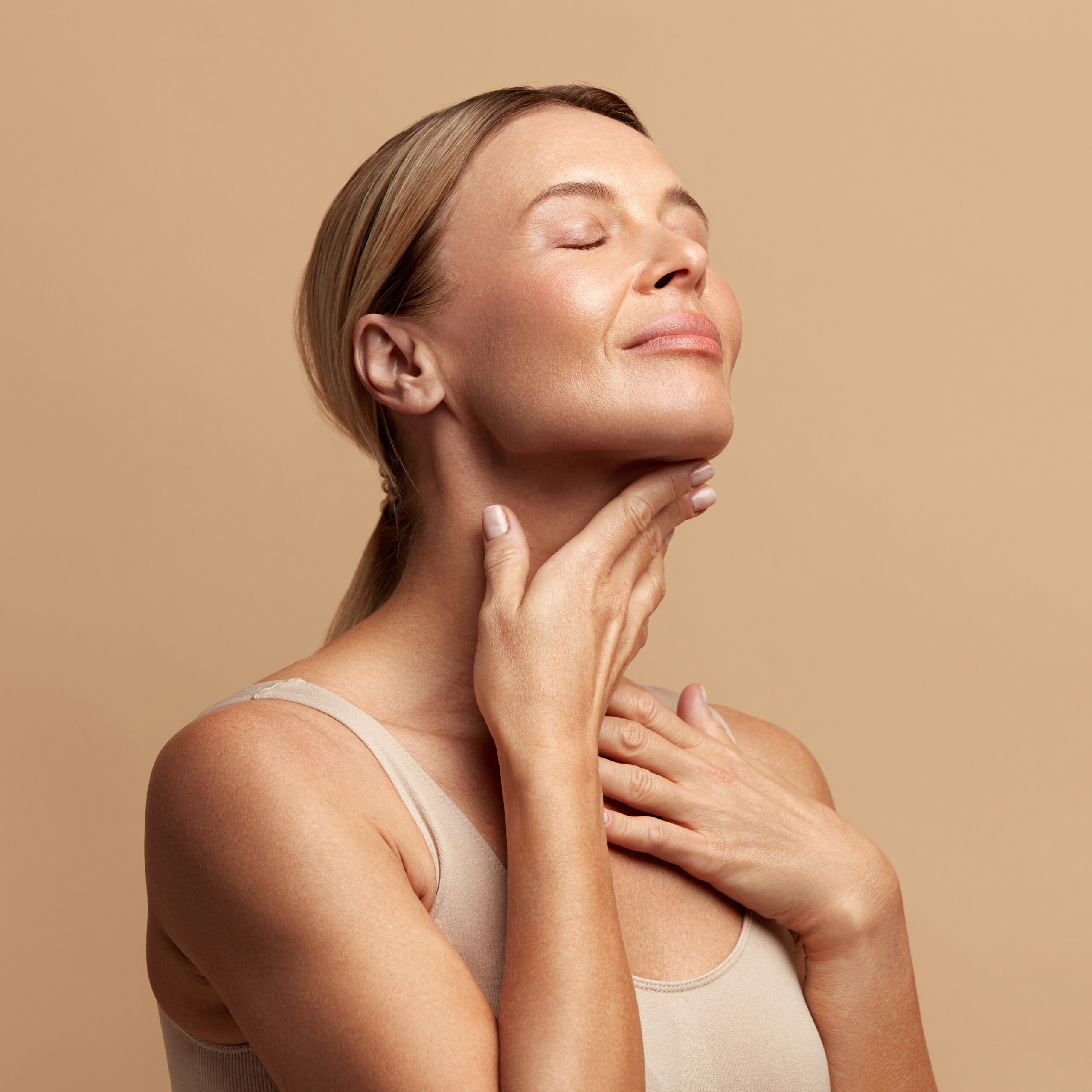 Woman gently touching her neck with eyes closed, displaying healthy skin and a calm, radiant appearance.
