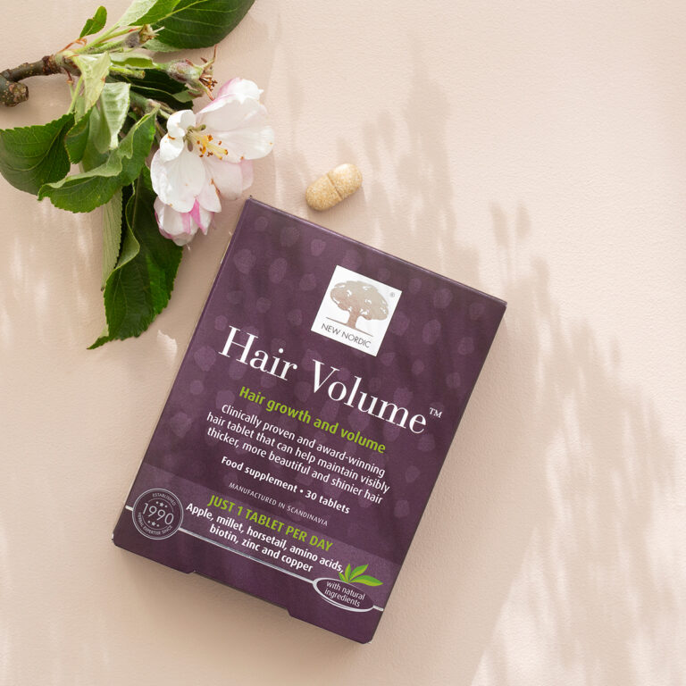 New Nordic Hair Volume™ package surrounded by apple flowers on a light background.