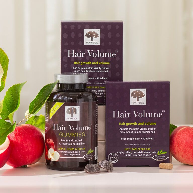 New Nordic Hair Volume™ gummies and tablets displayed on a surface, surrounded by fresh apples.