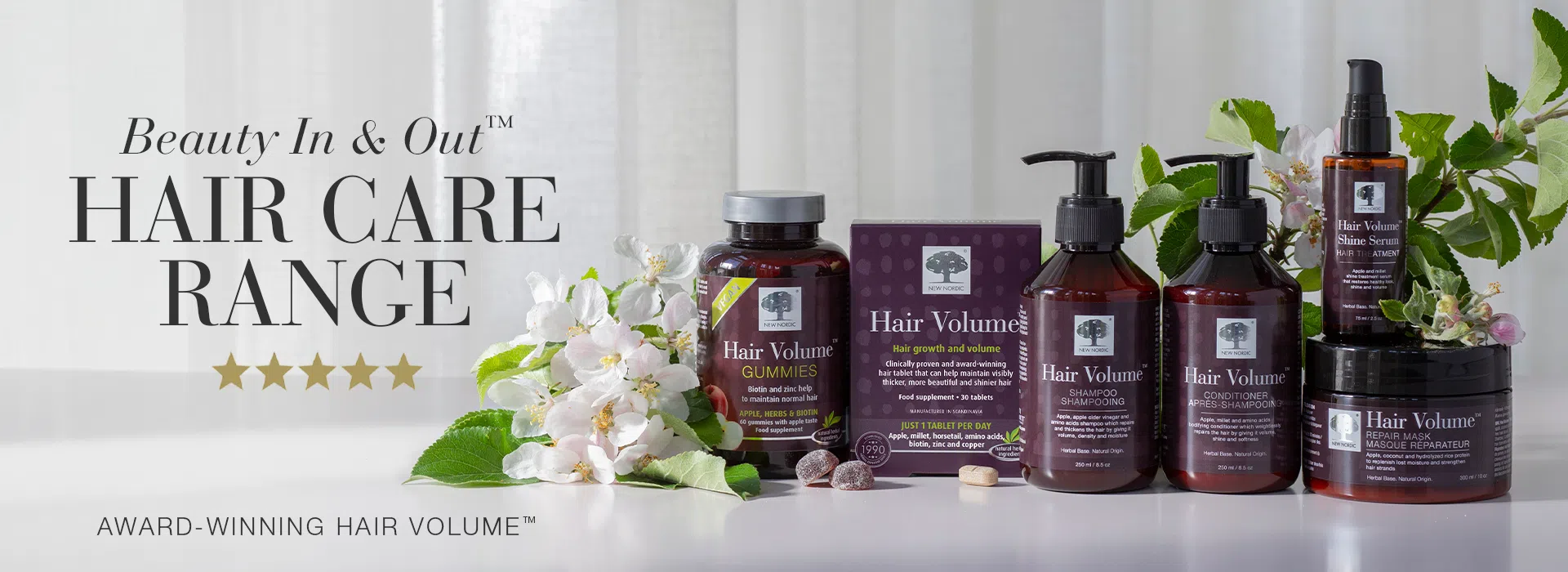 Banner showing the Beauty In & Out™ Hair Care Range, with Hair Volume gummies, supplements, shampoo, conditioner, serum and mask arranged with flowers and leaves.