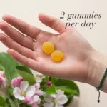 Hand holding 2 Apple Cider™ Gummies displayed with pink apple flowers and text Just 2 gummies per day.