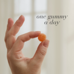 Hand holding a single orange Biotin™ Gummy displayed with text One gummy a day.