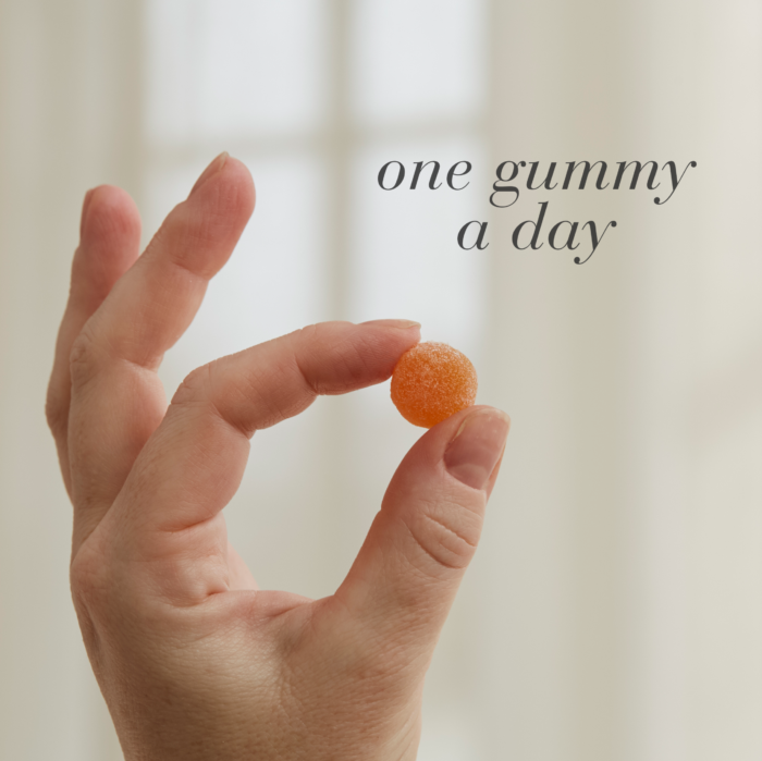 Hand holding a single orange Biotin™ Gummy displayed with text One gummy a day.