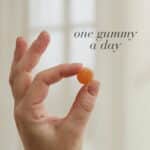 Hand holding a single orange Biotin™ Gummy displayed with text One gummy a day.