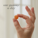 Hand holding a single orange gummy with text One gummy a day.