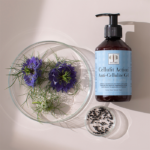 The Cellufit Action™ Anti-Cellulite Gel bottle displayed with dark purple flowers and cumin seeds in petri dishes.