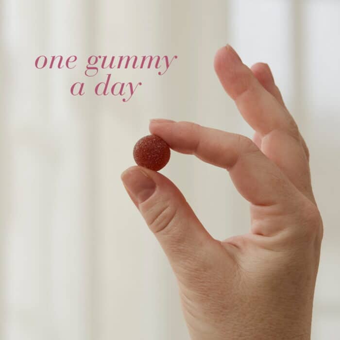 Hand holding a single Hair, Skin and Nail Strong™ Gummy with text One gummy a day.