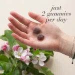 Hand holding two Hair Volume™ Gummies displayed with text just 2 gummies per day.