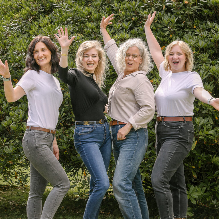 Four women smiling together in a cheerful setting.