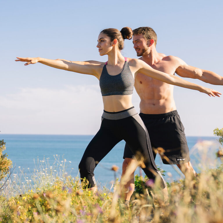 Couple practicing yoga together overlooking the ocean, enjoying fitness and mindfulness outdoors.