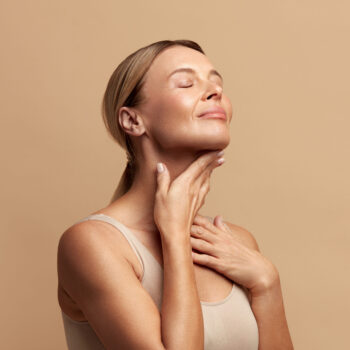 Woman gently touching her neck with eyes closed, displaying healthy skin and a calm, radiant appearance.