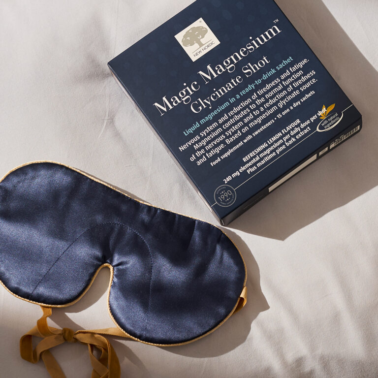 Magic Magnesium Glycinate shot pageing laying on a bedsheet with a sleep mask next to it
