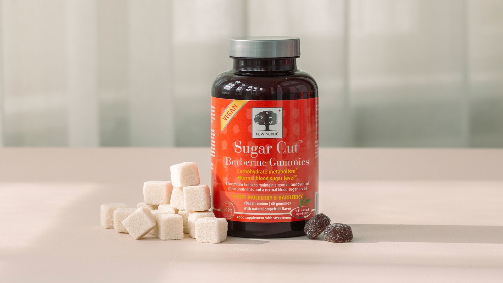 A glass of Sugar Cut Berberine Gummies next to a pile of sugarcubes and 2 gummies