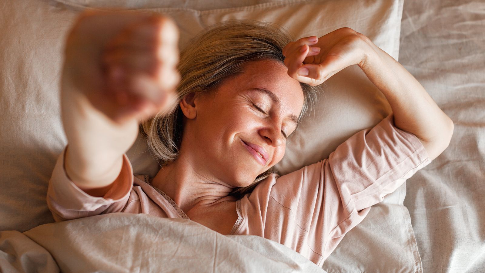 Magic Magnesium™ Glycinate 16 A woman lying in bed, stretching her arms and smiling, looking relaxed.