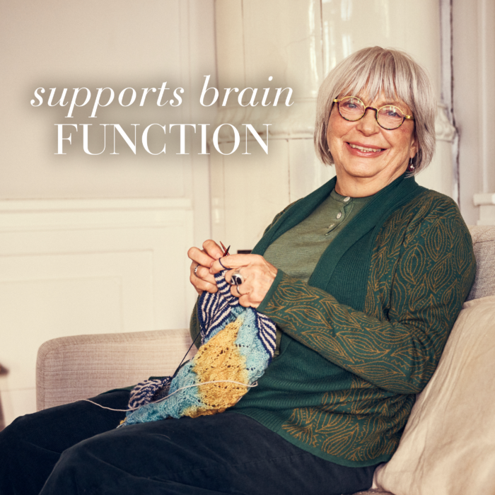 Older happy lady sitting on the sofa doing knitting