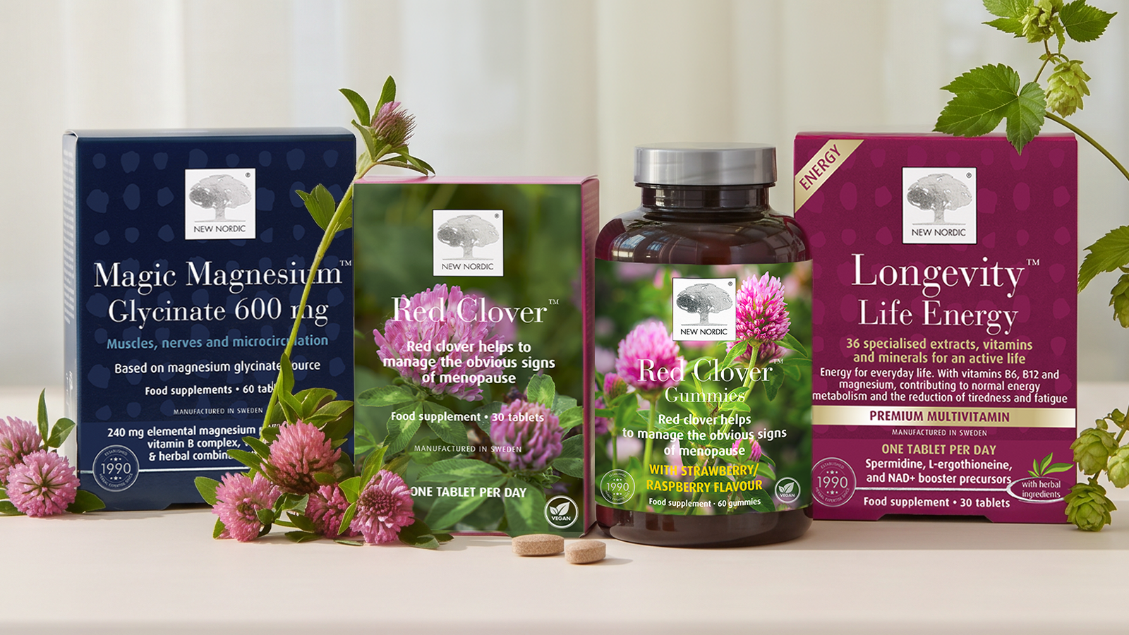 Four products of New Nordic lined up, magnesium glycinate, red clover tablets, red clover gummies and longevity life energy with some flowers and herbs around