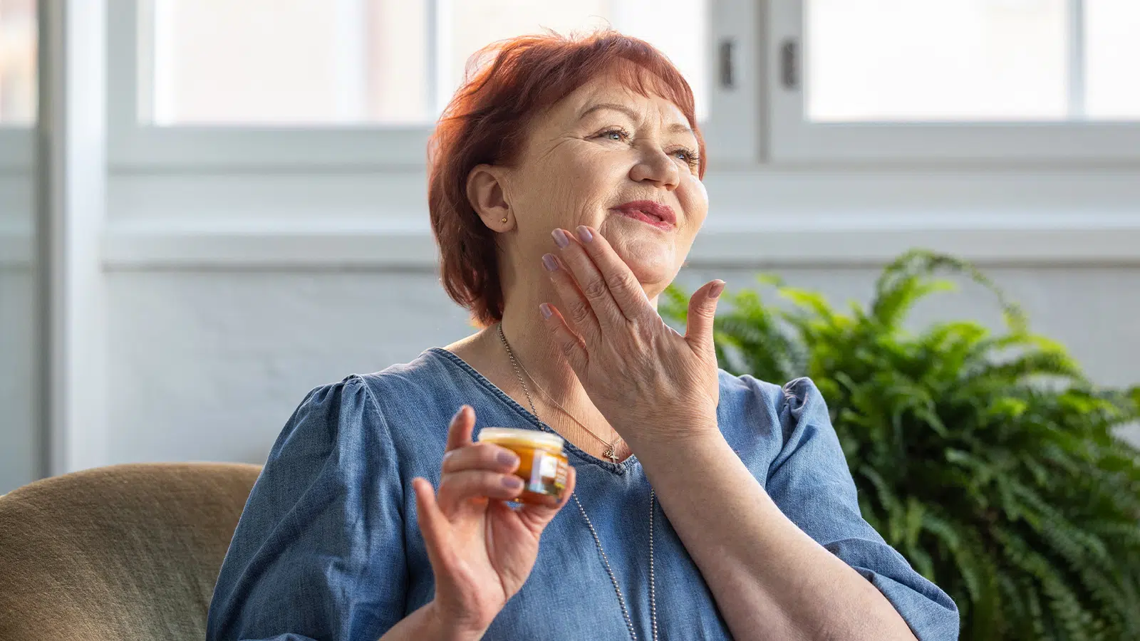 Older woman smiling whilst putting some cream on her face
