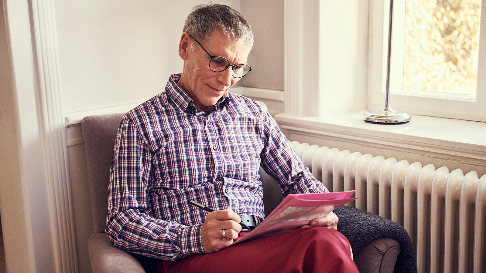 Older man sat down doing a brain puzzle in a magazine with a pen in his hand