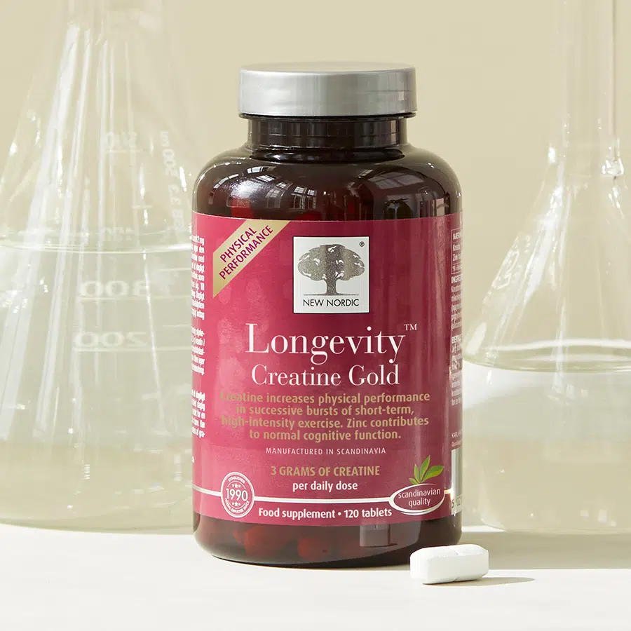 New Nordic Longevity™ Creatine Gold food supplement displayed with laboratory glassware and a tablet.