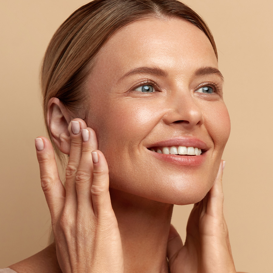 Smiling woman gently touching her face, showing smooth and radiant-looking skin.