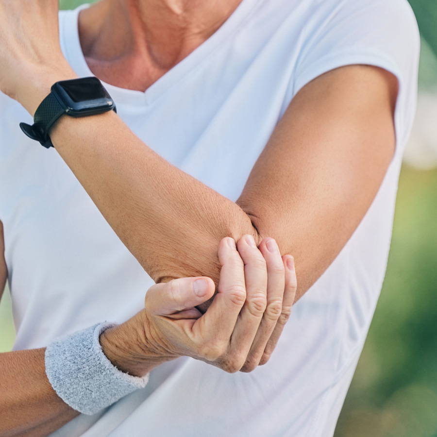 Person in sportswear holding their elbow while wearing a smartwatch and wristband.