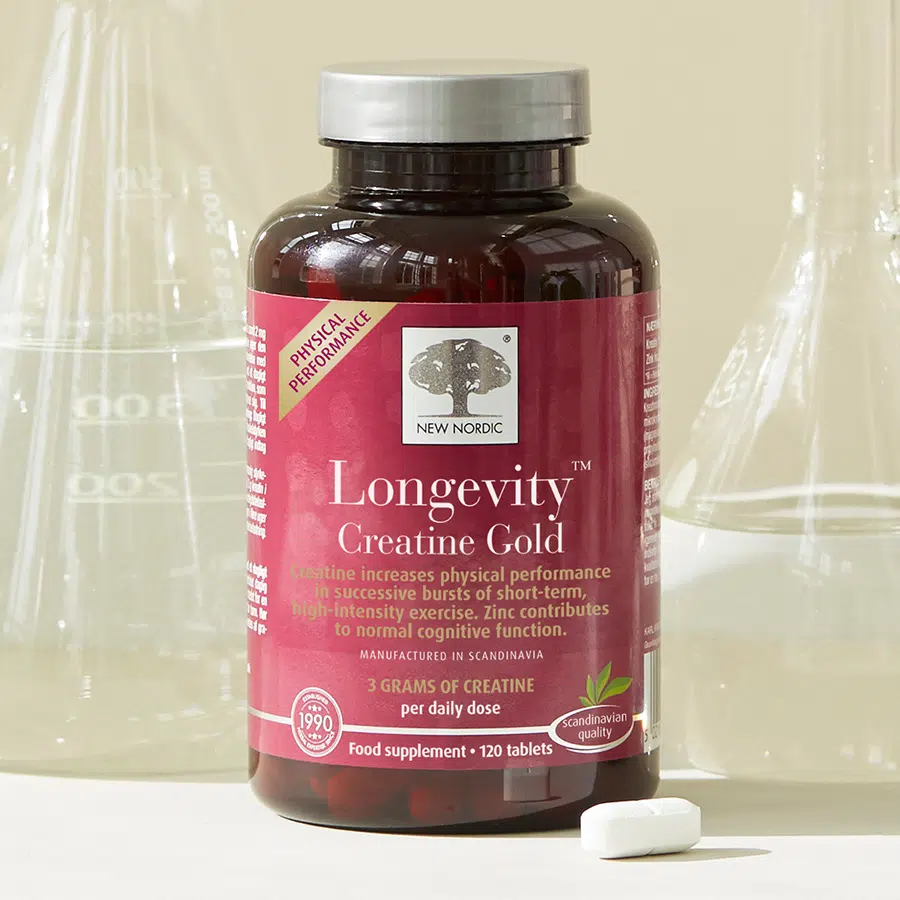 New Nordic Longevity™ Creatine Gold food supplement displayed with laboratory glassware and a tablet.