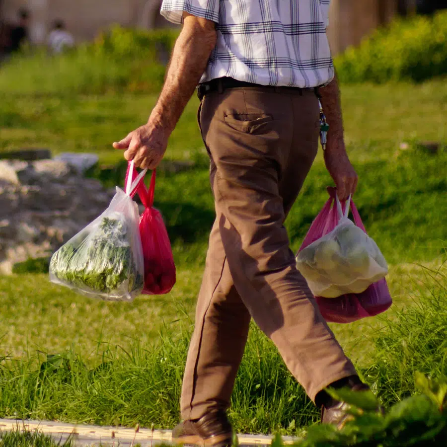 Older man walking outdoors while carrying several bags of groceries.