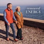 Older couple walking hand in hand along a rocky seaside path, with the text “renewed energy”.